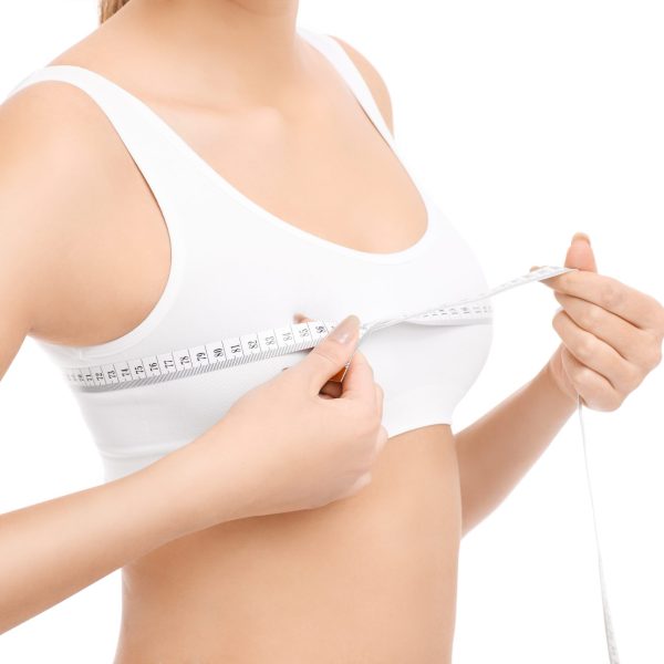 A picture of a fit woman with tape measure checking her bust over white background